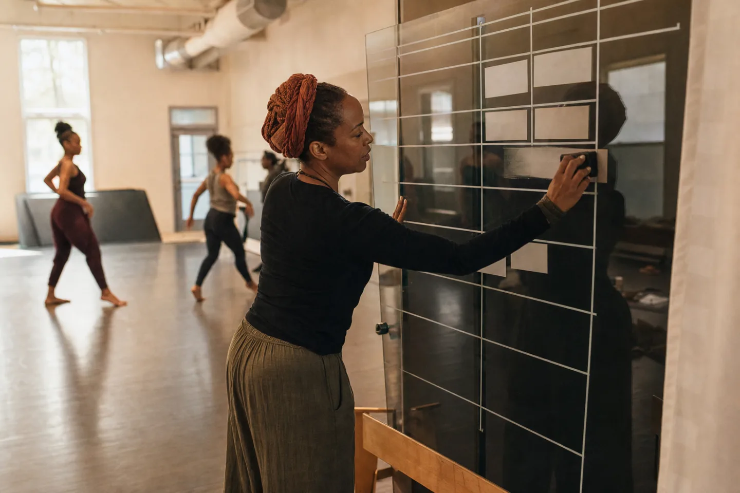 Amina erases one tutoring session from a glass schedule board as students work nearby.