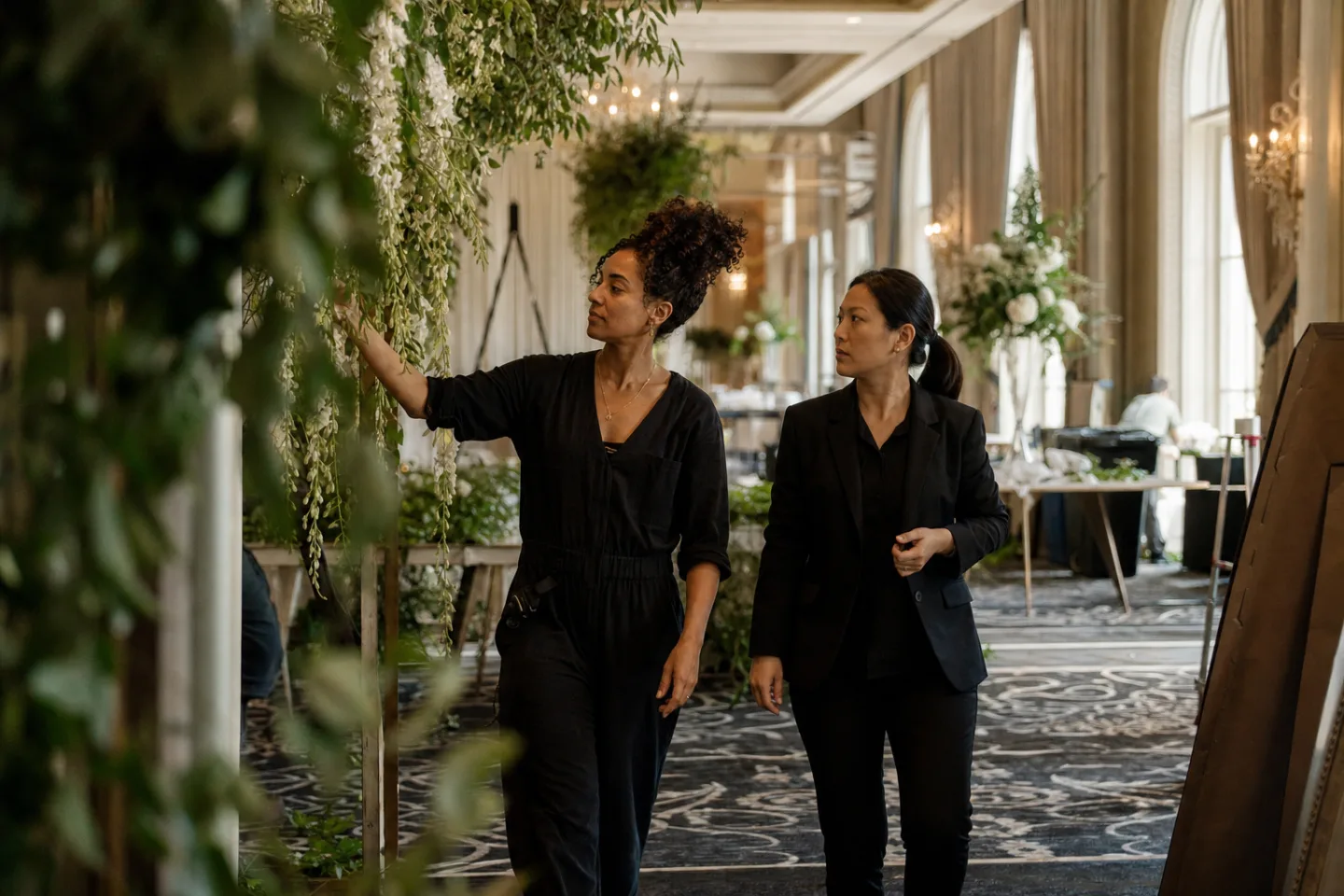 Amara and a hotel events manager walk through a ballroom floral installation.