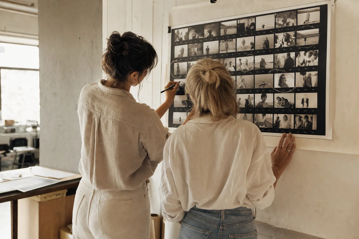 Sofia and Maya mark a large contact sheet mounted on a photography studio wall.