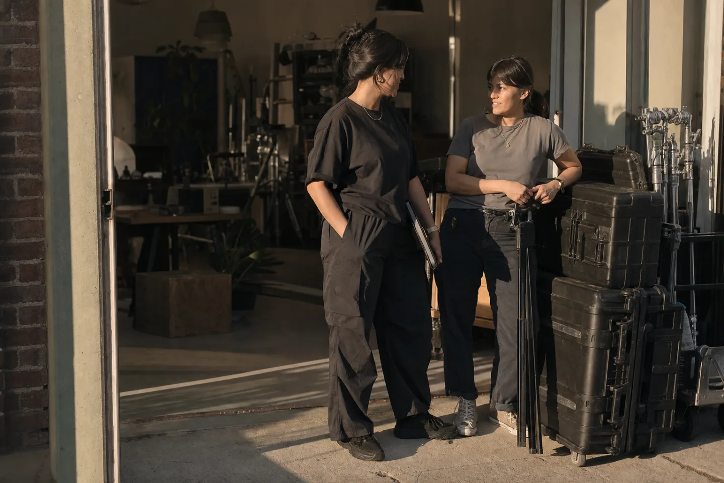Sofia gives Maya a final portfolio beside packed production cases at the studio doors.